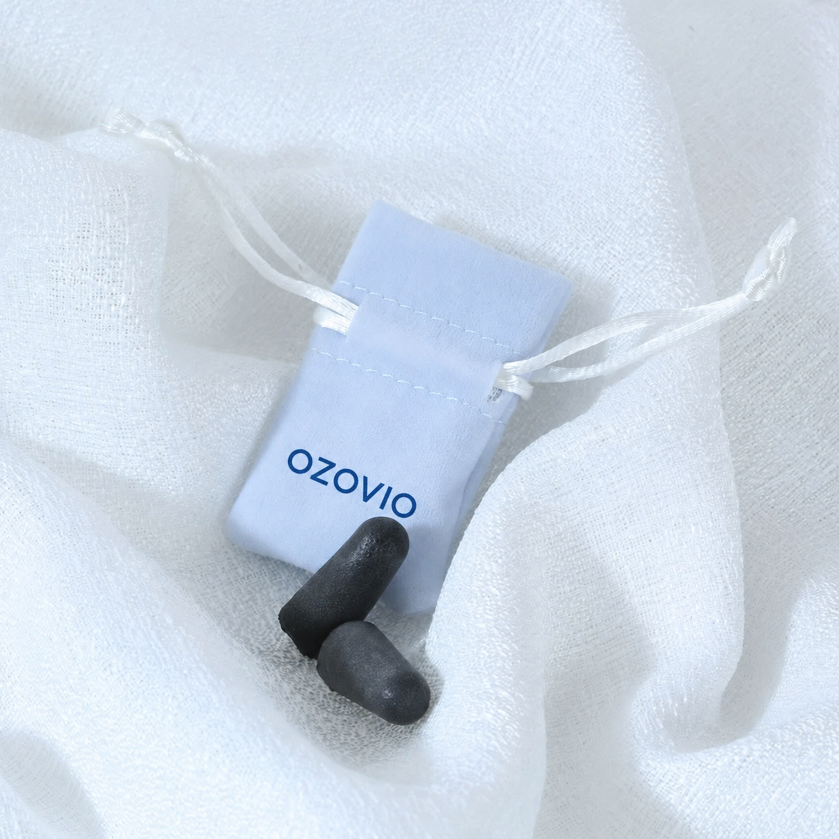 Tapones antirruido OZOVIO de espuma con su bolsa de tela azul claro sobre una sábana blanca